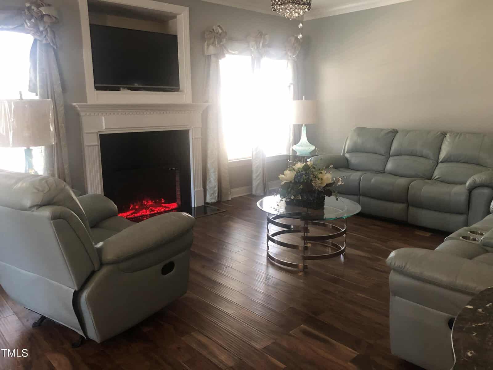 Elegant living room with gray walls and hardwood floors, featuring two gray sofas, a modern glass coffee table, and an electric fireplace under a mounted tv.