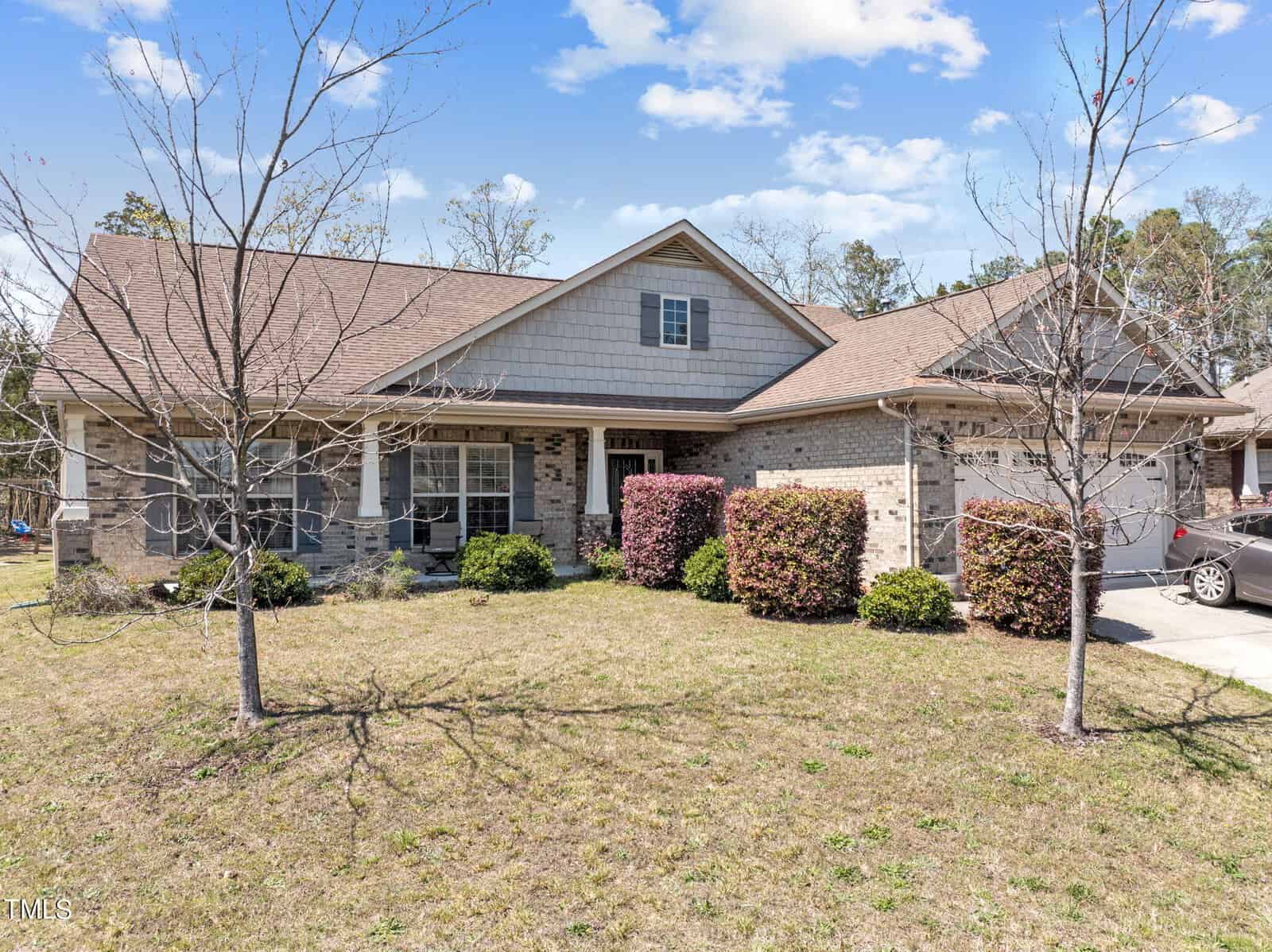 A charming single-story brick house on 1162 Phelps Court features a gabled roof and is surrounded by a front yard with leafless trees and bushes. The partly cloudy skies add to the serene atmosphere. A driveway, perfect for easy access, is visible on the right side.