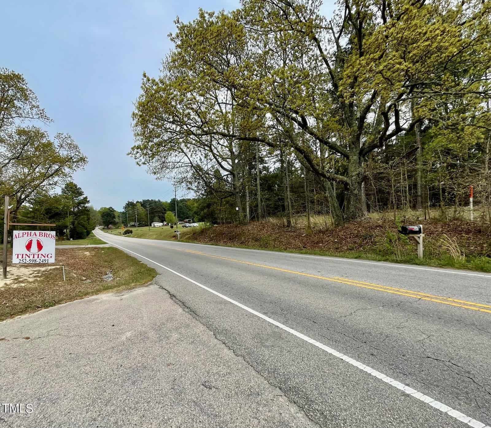 A rural road stretches into the distance, flanked by trees on either side and a "lepley bros. trucking" sign on the left. there's a mailbox near the sign, under a clear sky.
