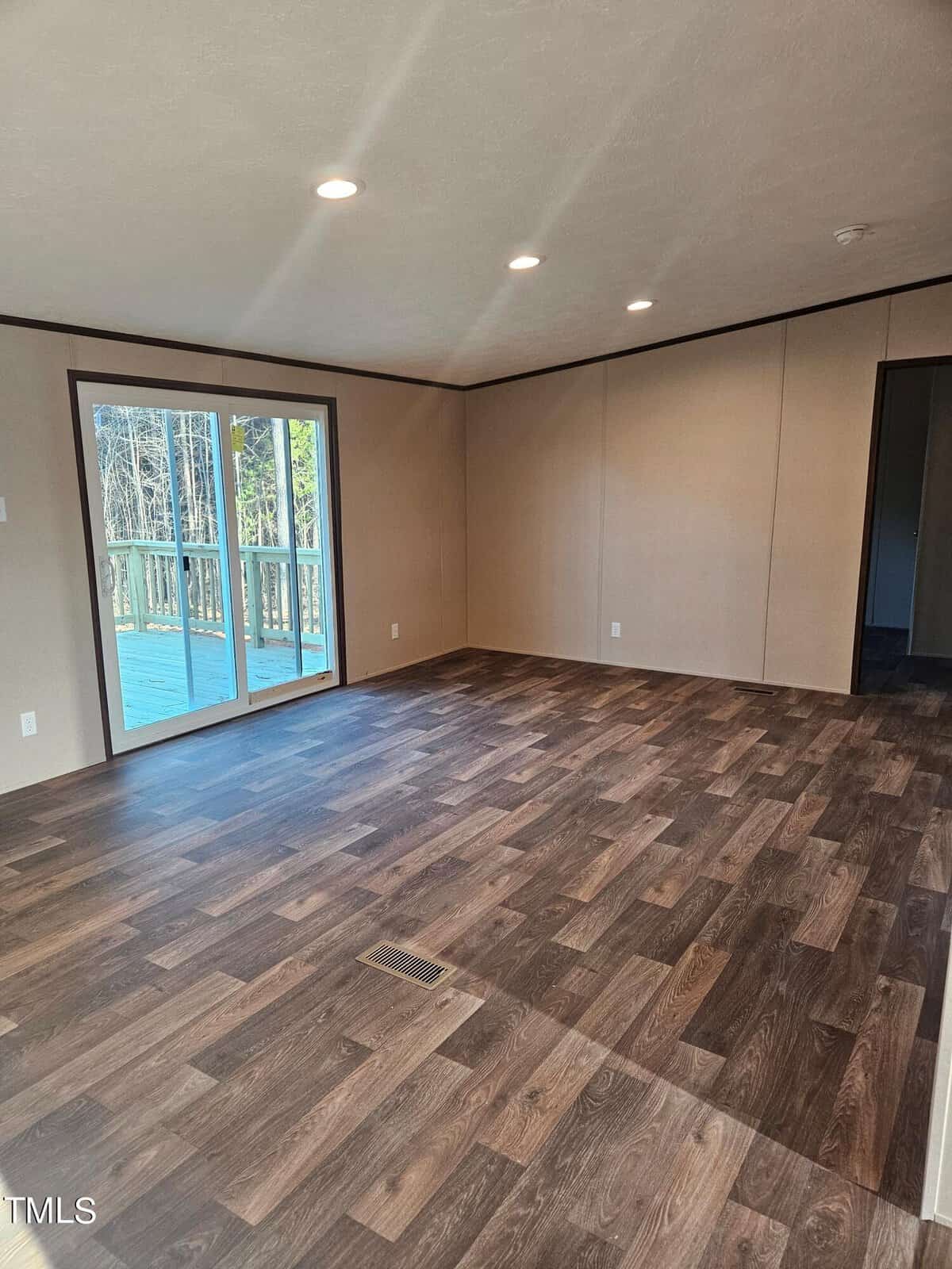 Empty room with dark wooden flooring, beige walls, and a large sliding glass door leading to a balcony with a view of trees.