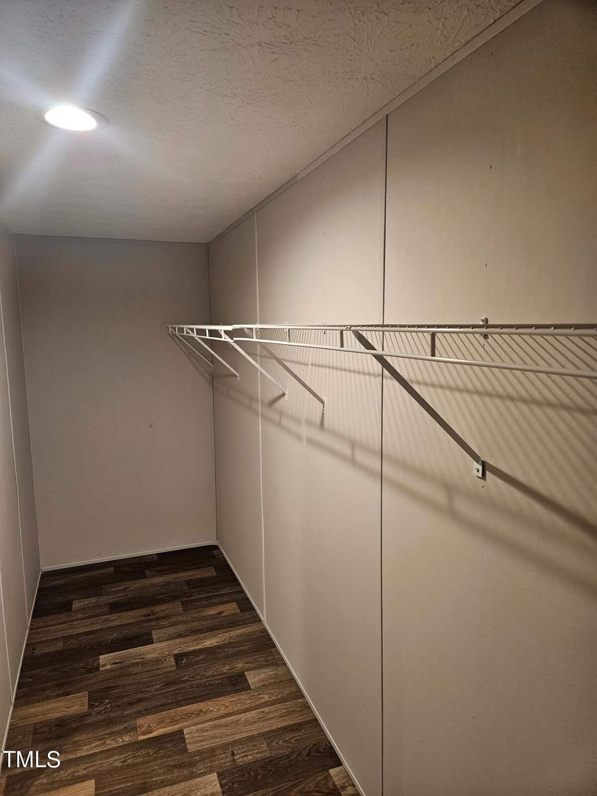 An empty walk-in closet with wooden flooring and built-in white wire shelving along the walls, illuminated by overhead led lights.