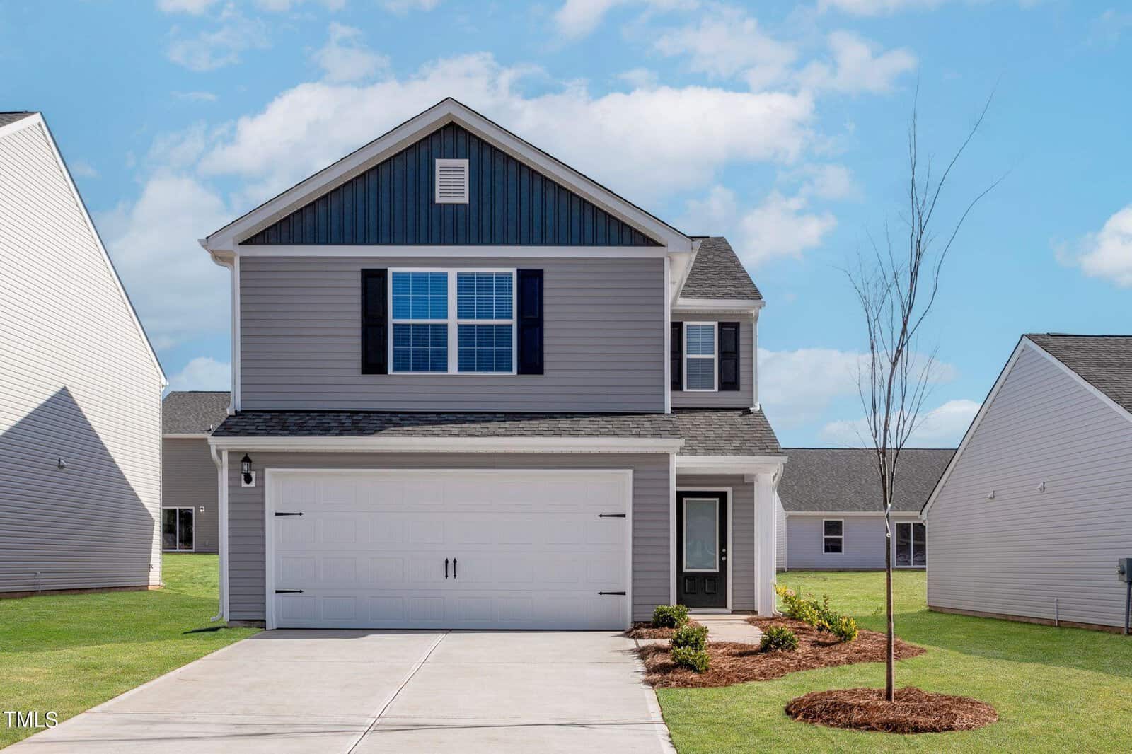 A modern two-story house at 506 Rhino Bend, Oxford, with gray siding, black shutters, and a double garage. The front yard features a young tree, fresh landscaping, and a concrete driveway under a blue sky with scattered clouds.