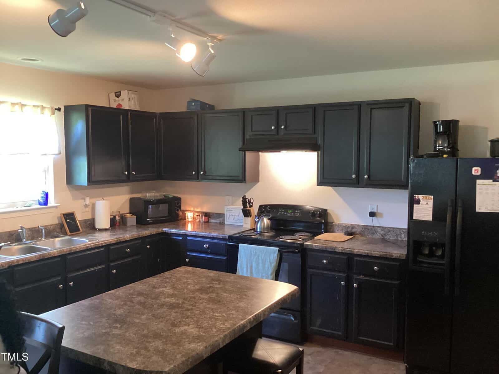 A well-lit kitchen with dark cabinets, matching appliances, and granite countertops. there is a central island and modern lighting fixtures. .