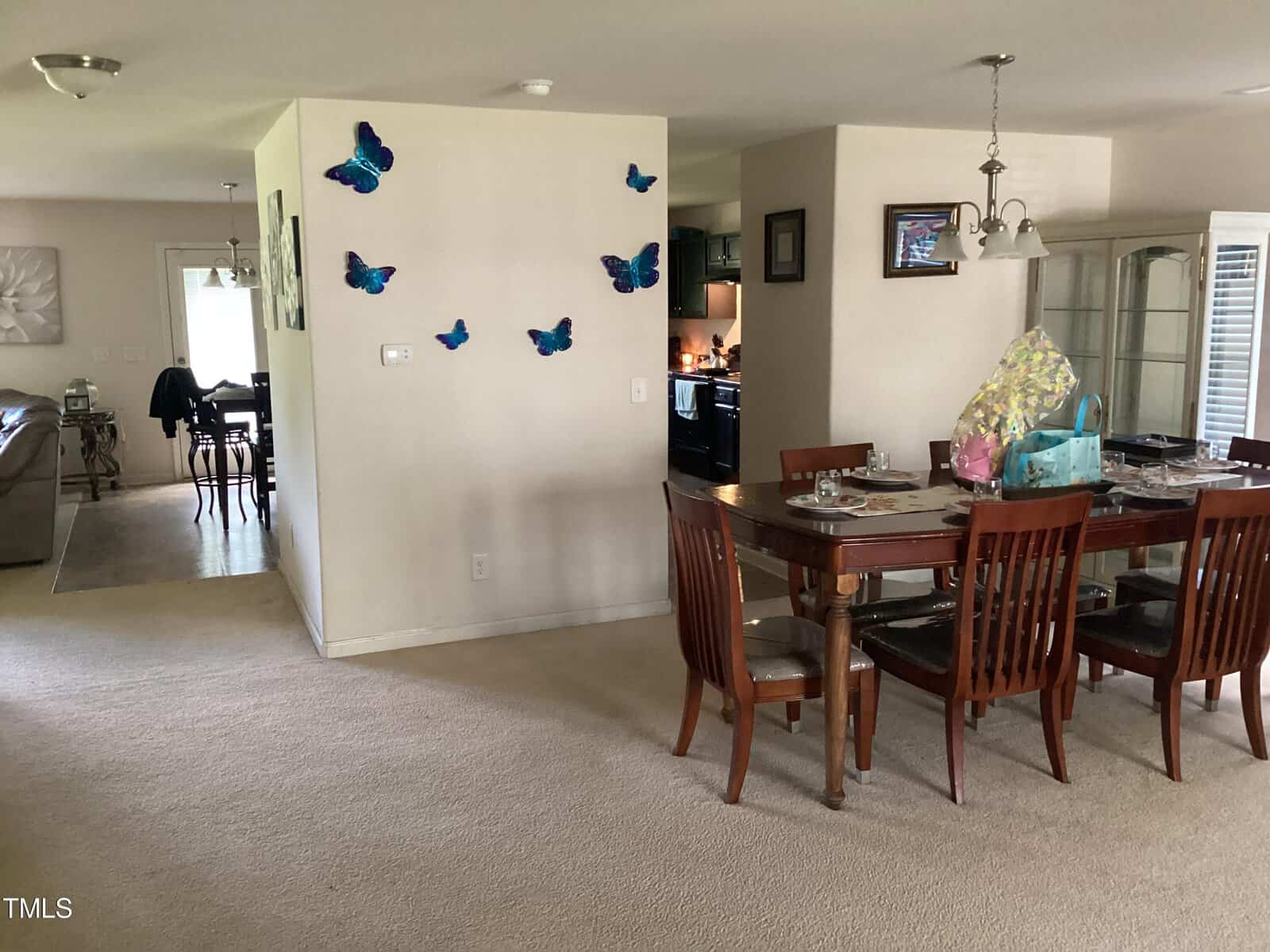 A spacious living area with a dining table set for a meal, butterfly decorations on a wall, and an adjacent kitchen. the room has a welcoming, lived-in feel.