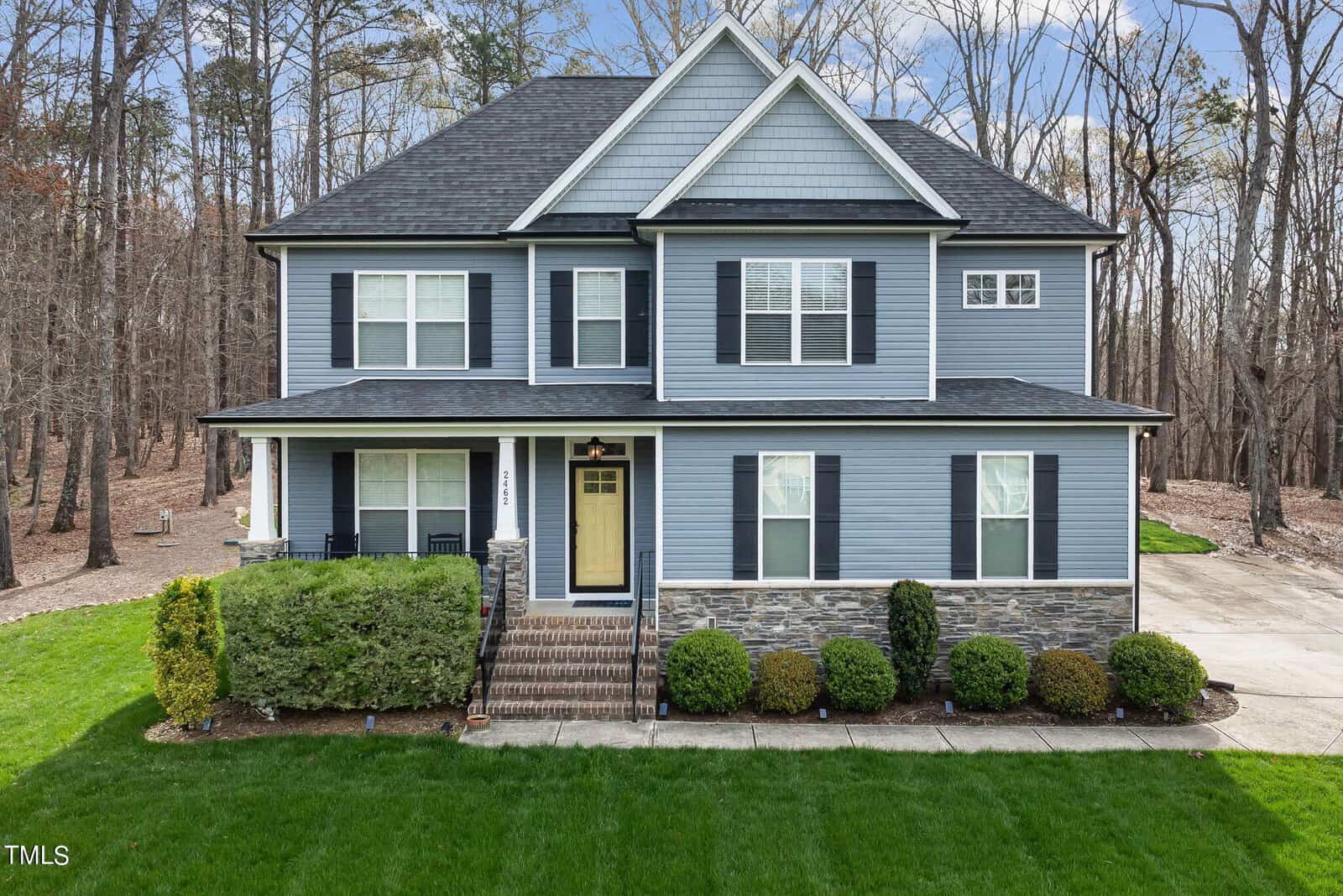 Nestled in the serene woods of Franklinton, the two-story house at 2462 Golden Forest Drive features gray siding, white trim, and a stone facade. A neatly manicured lawn frames this charming home, complete with a small front porch adorned with columns.