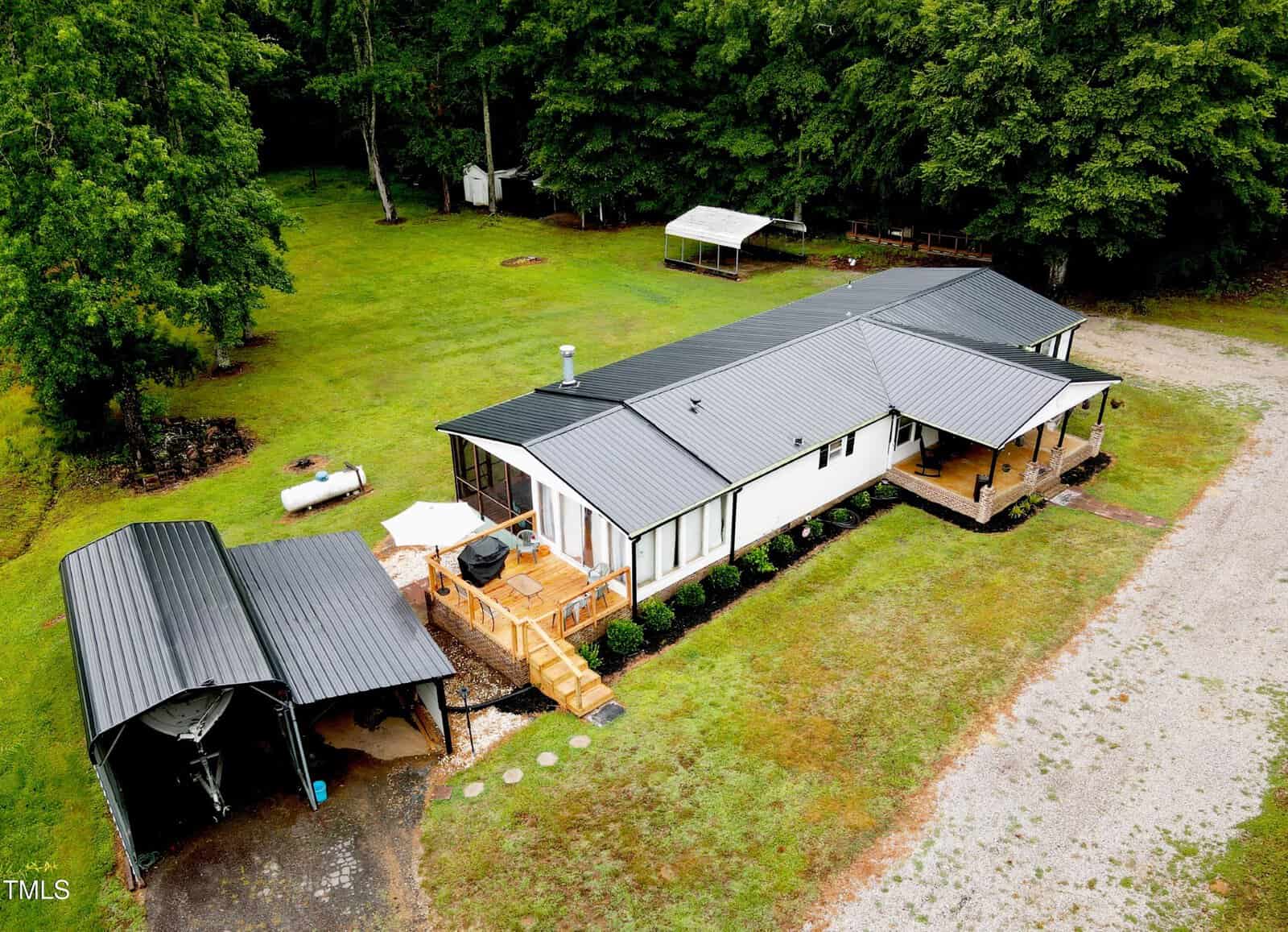 Aerial view of a large single-story house with metal roofs, surrounded by green grass. there are multiple covered areas and a driveway leading up to the house.