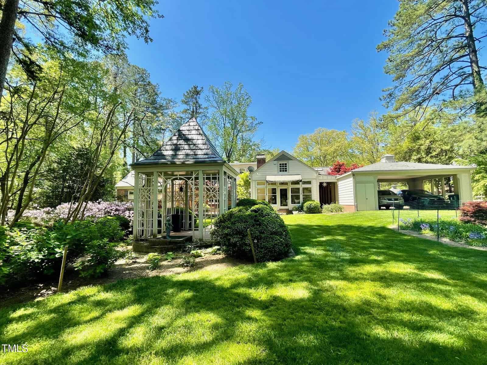 A picturesque suburban home with a lush green lawn and vibrant flowers, featuring a gazebo on the left and an attached garage on the right. bright sunlight and tall trees compose the background.