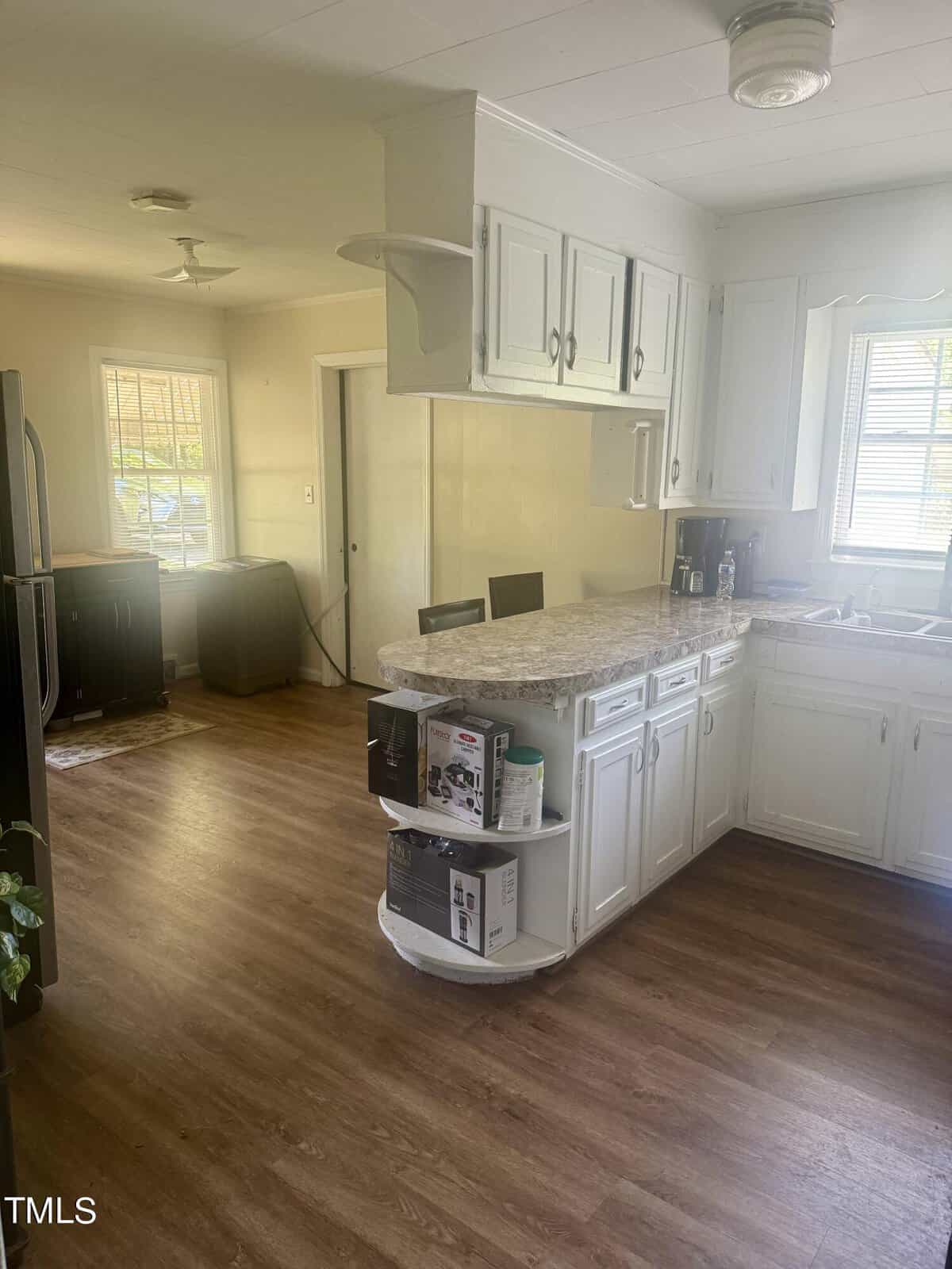A bright kitchen with white cabinetry, granite countertops, and stainless steel appliances. there’s a center island and hardwood flooring, with natural light coming through windows.
