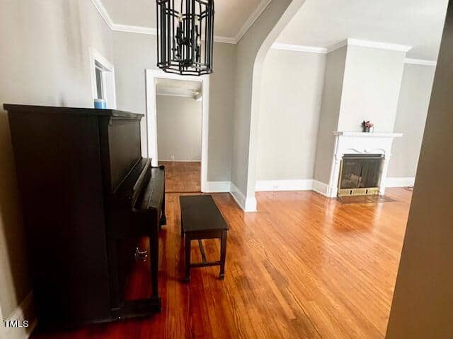 A spacious living room with polished hardwood floors, a black upright piano, a matching bench, and a tall white fireplace. Light gray walls and white molding provide a modern touch, and a geometric black chandelier hangs from the ceiling.