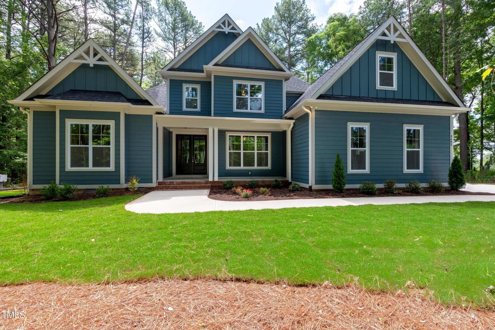 Nestled on 3602 Horseshoe Road in Creedmoor, this charming two-story house boasts blue siding and white trim, with multiple gables and large windows. A covered porch invites you to enjoy the landscaped lawn, all beautifully framed by tall trees.