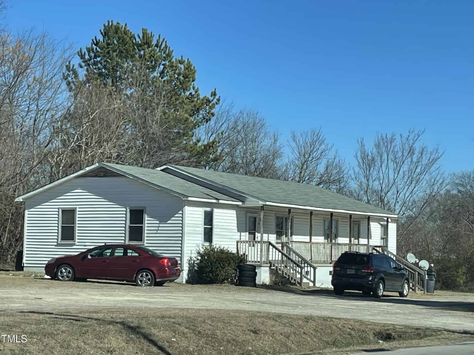 A white single-story modular home at 101 Mason Street, Henderson NC, with a covered front porch, flanked by two parked cars, a red sedan and a black suv, in a grass