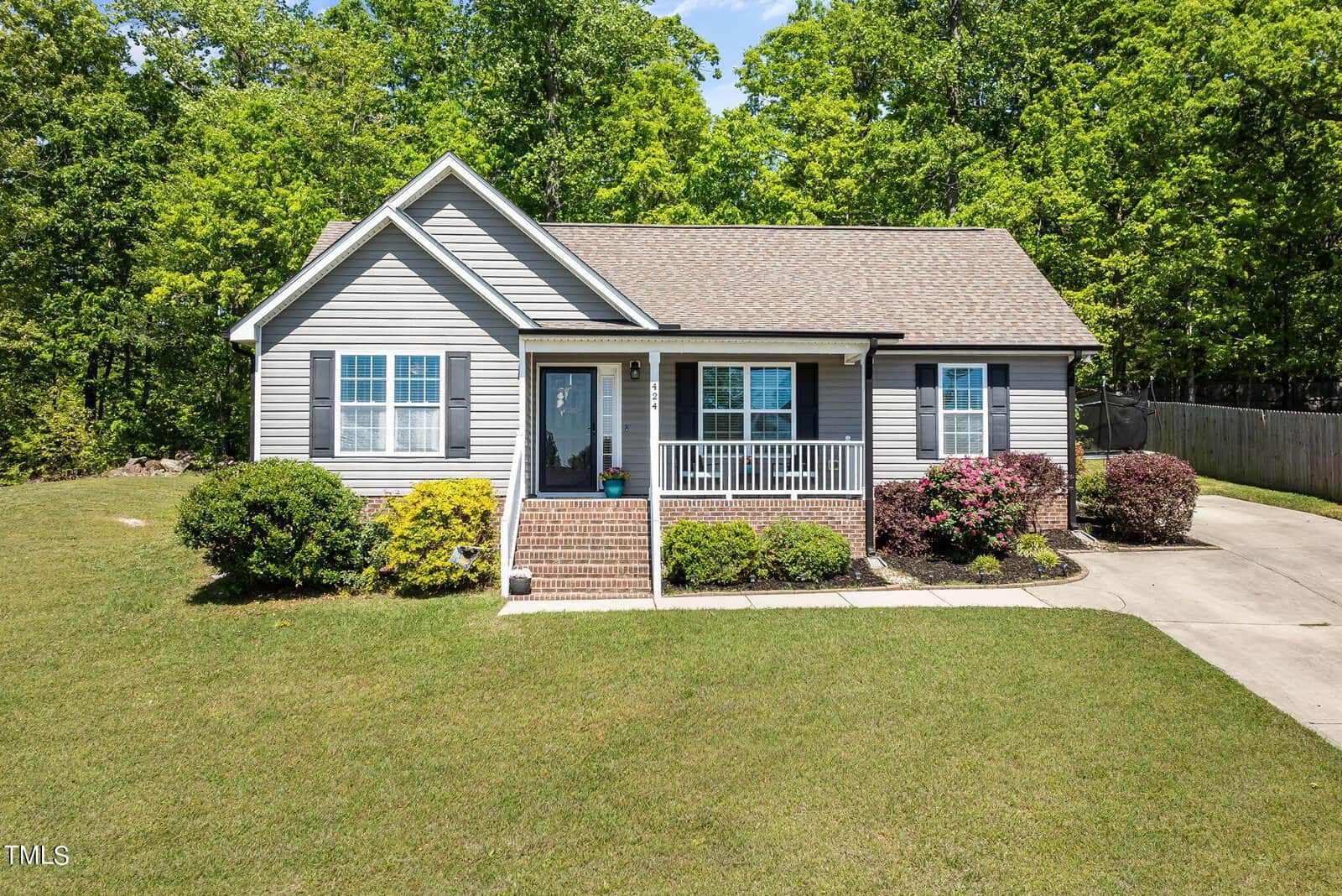 Nestled at 424 Angus Place, this quaint single-story house with gray siding and a brown roof features a small front porch with white railings. Surrounded by a well-maintained lawn, the charming landscape includes shrubs and trees under a clear blue sky.