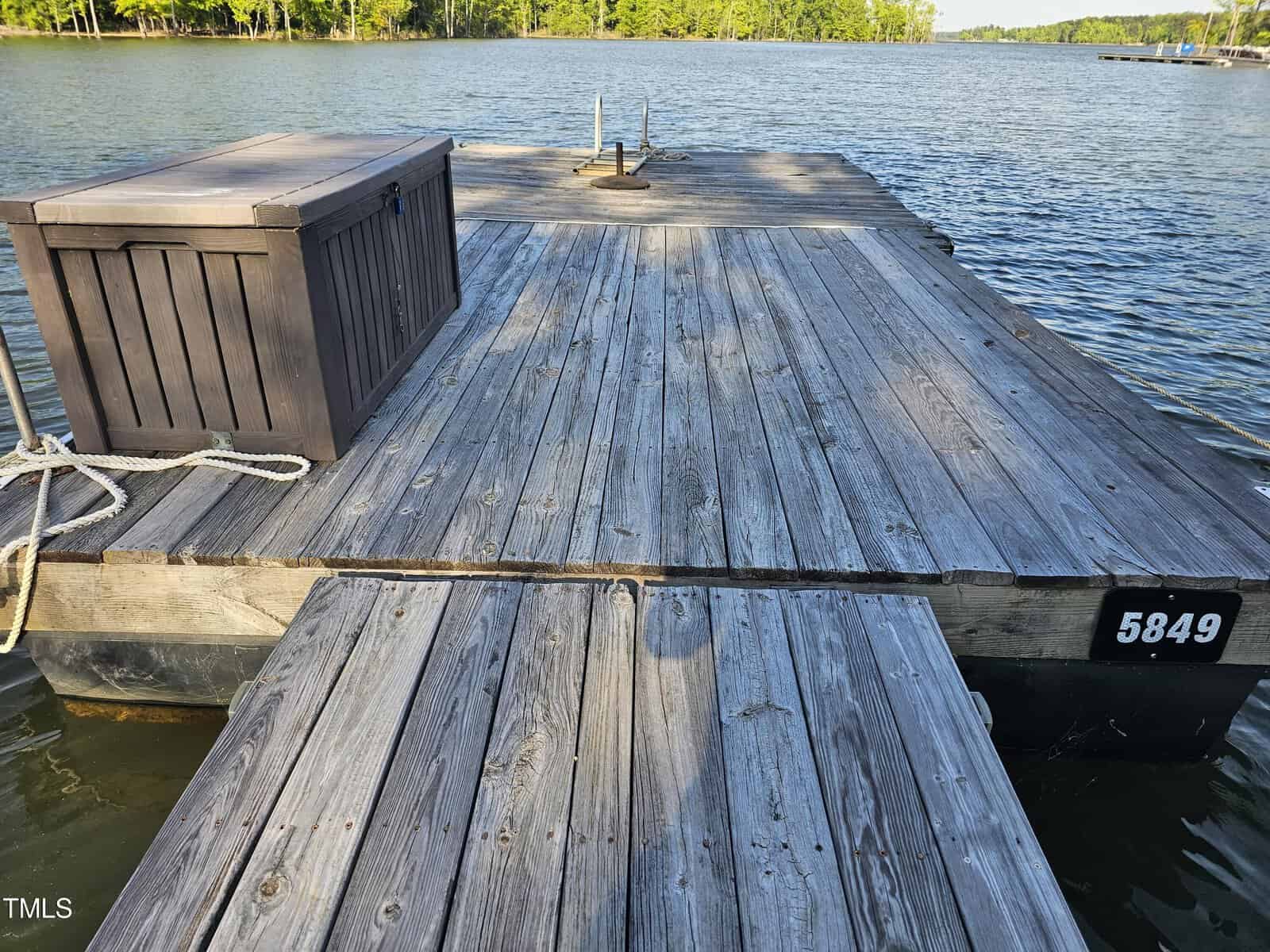 Wooden dock on a calm lake with a storage box and a roped swim ladder. the dock number 5849 is visible on the side.