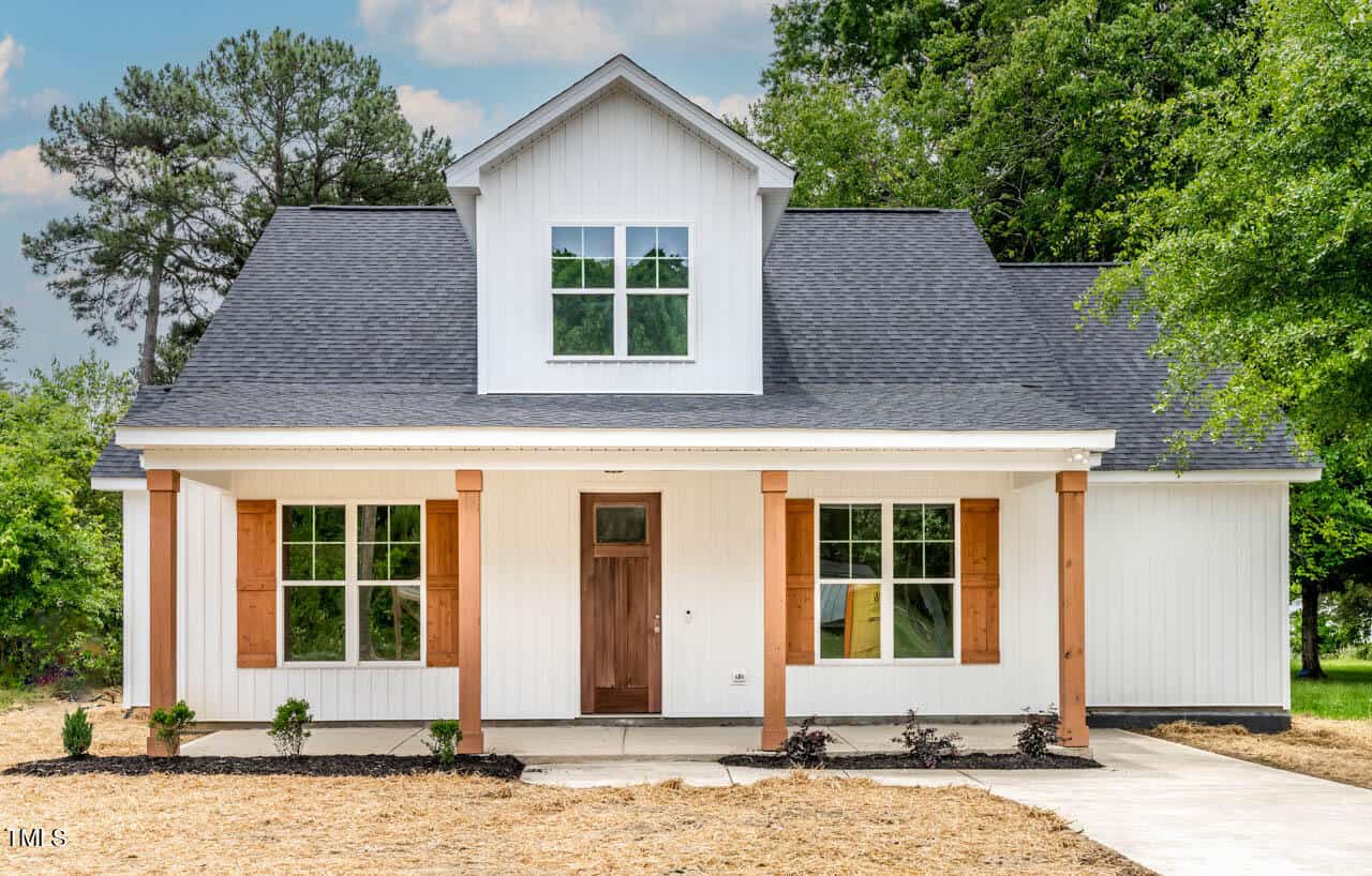 Located at 205 Rogers Avenue in Creedmoor, this white, modern farmhouse-style home boasts a striking black roof and a welcoming front porch with wooden columns. Large windows and a brown wooden front door are complemented by a newly planted garden and fresh landscaping.
