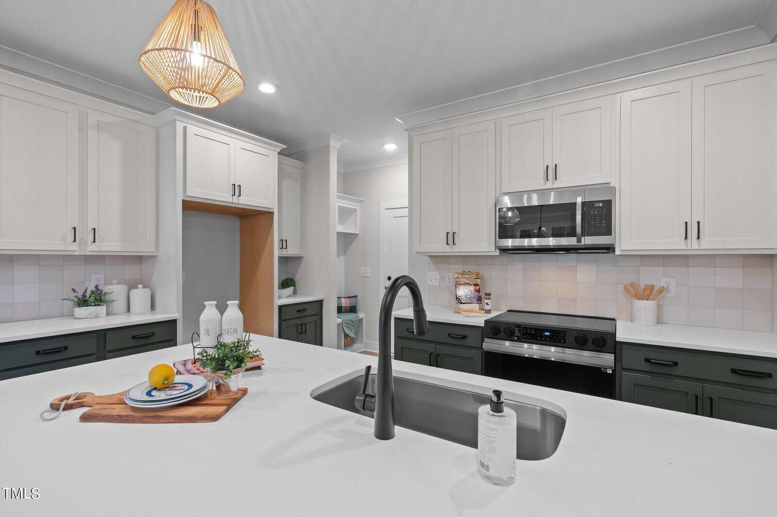 Modern kitchen with white cabinets, dark lower drawers, a built-in microwave above the stove, and a central island featuring a sink, faucet, soap dispenser, and a wooden tray with decorative items and food.