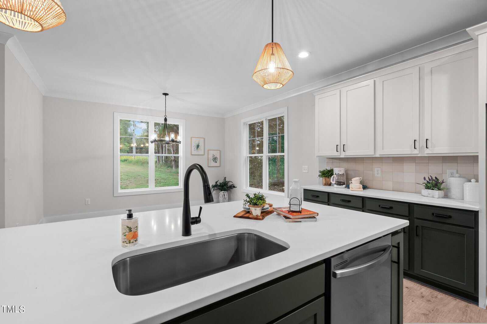 Modern kitchen with a black faucet on a white island, black lower cabinets, white upper cabinets, pendant lights, and large windows letting in natural light; a bright, tidy, and inviting space.