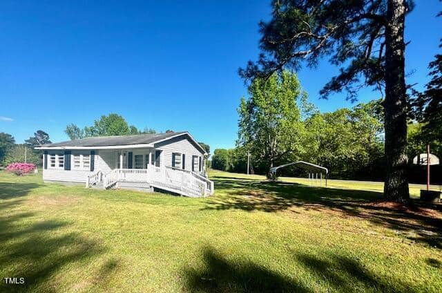 A small, light gray house with a porch sits on a large, grassy lawn surrounded by trees at 5086 Antioch Road. The sky is clear and blue, and there's a basketball hoop to the right near a metal carport in Oxford.