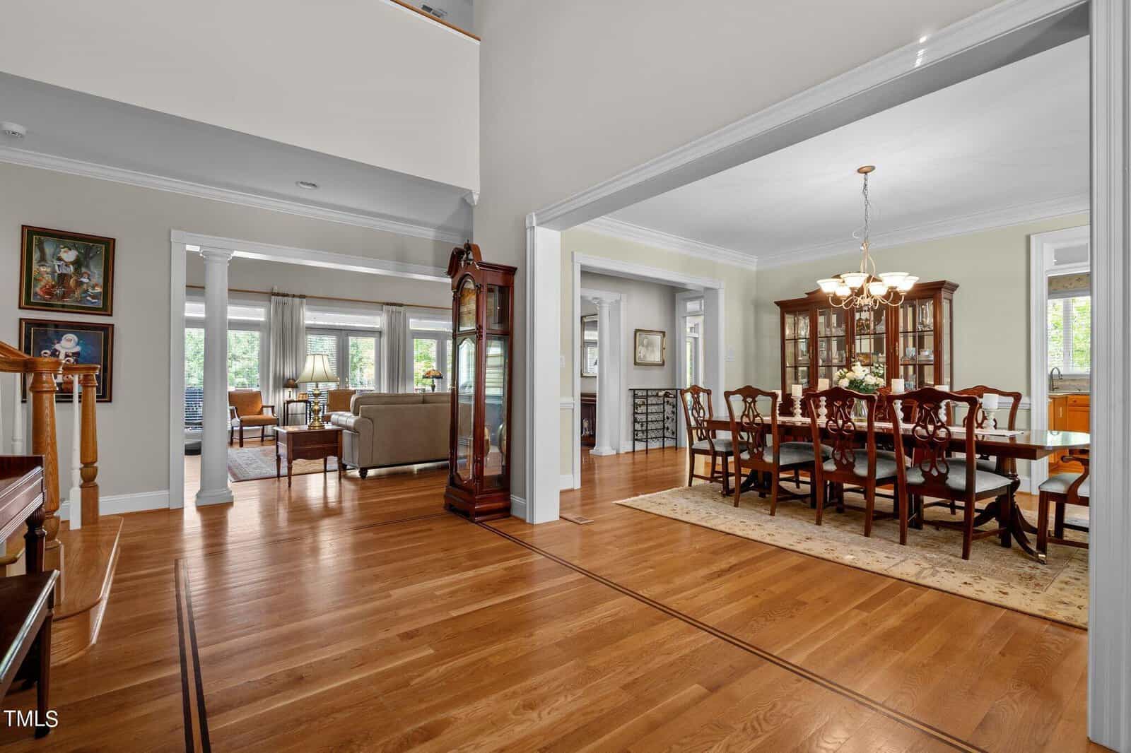 Spacious interior with a formal dining area featuring a wooden dining table and chairs, chandelier, and china cabinet. Adjoining room has a sitting area with sofas. Hardwood floors and large windows provide a warm, inviting atmosphere.
