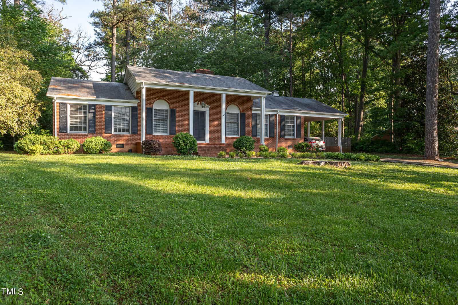 A charming brick house with white columns and windows at 1610 Parker Lane, surrounded by lush green grass and trees bathed in soft sunlight.