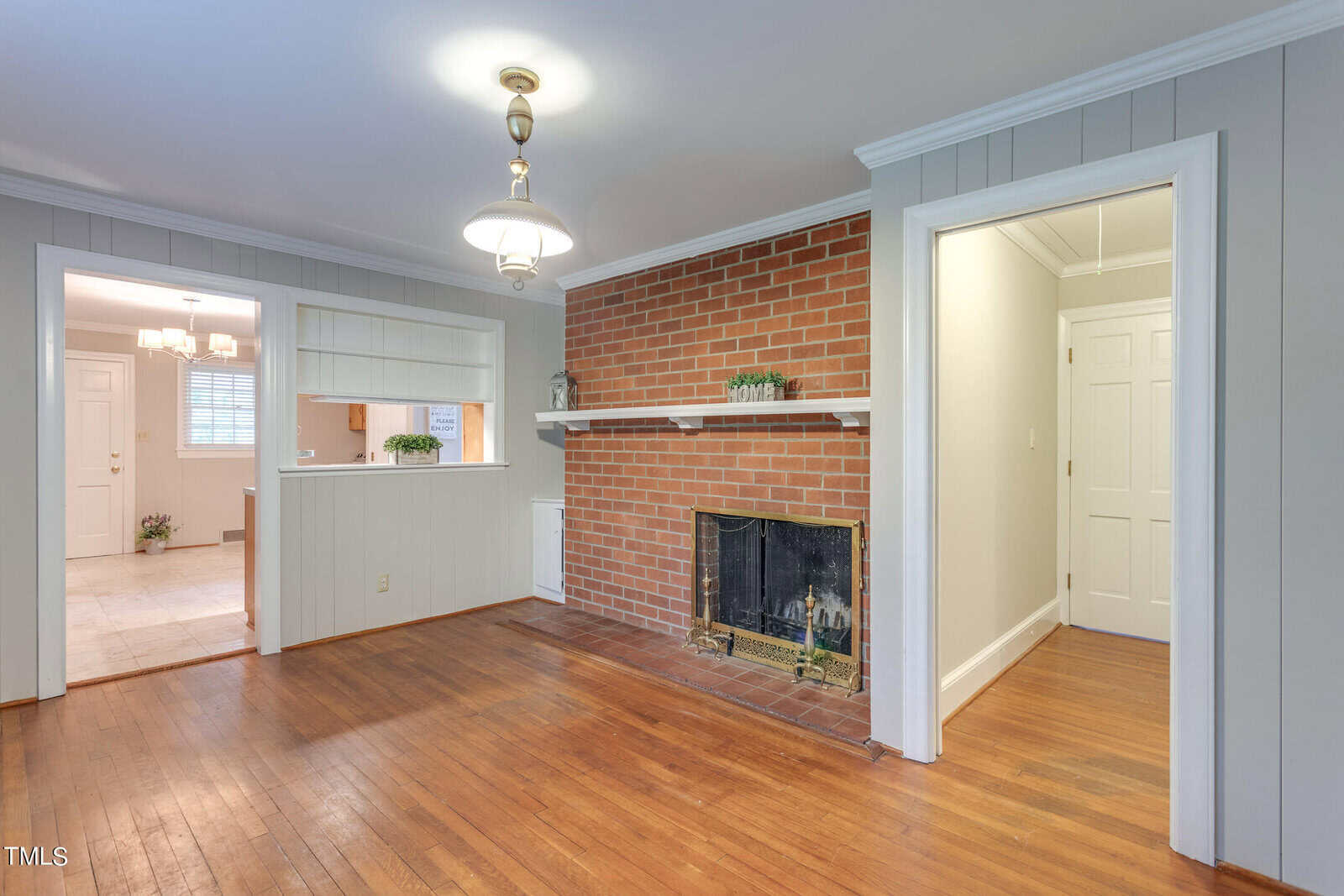 Spacious room featuring hardwood floors, a red brick fireplace, white walls with decorative molding, and doorways leading to adjacent rooms.