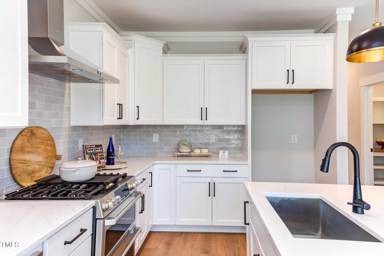 Modern kitchen with white cabinets, stainless steel appliances, a gas stove, black faucet, and a marble countertop. Wooden floor and open shelves with dishes and decor add a clean, inviting atmosphere.
