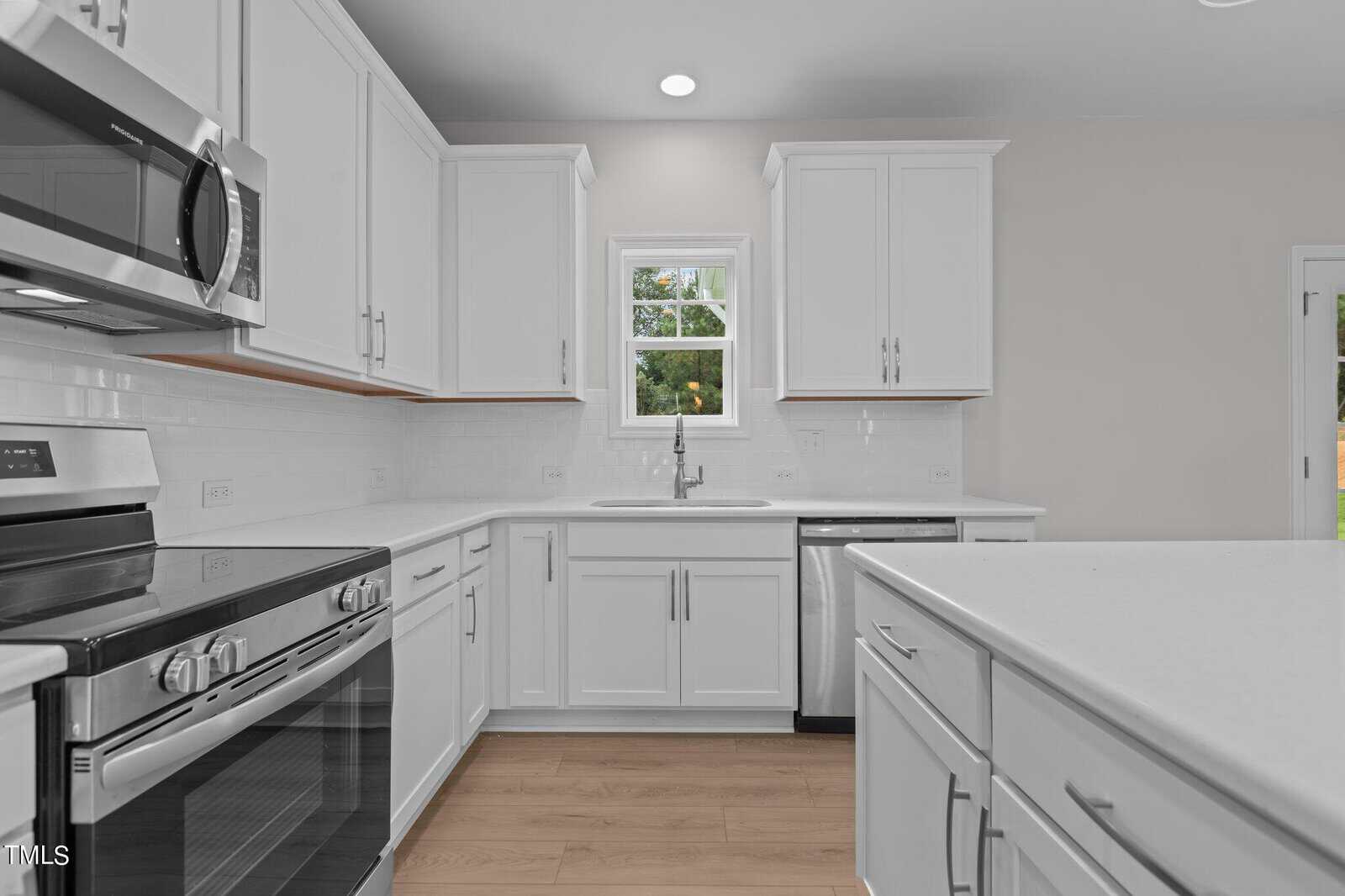 Modern kitchen with white cabinets, stainless steel appliances, a large island, light wood flooring, and a window above the sink letting in natural light.