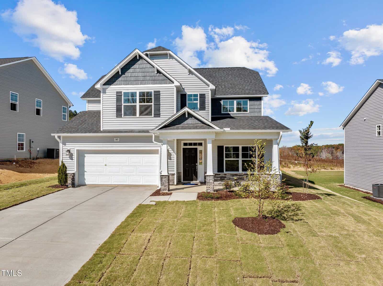A two-story modern suburban house with gray siding, white trim, a covered front porch, and attached two-car garage, set on a freshly landscaped lawn under a blue sky with scattered clouds.