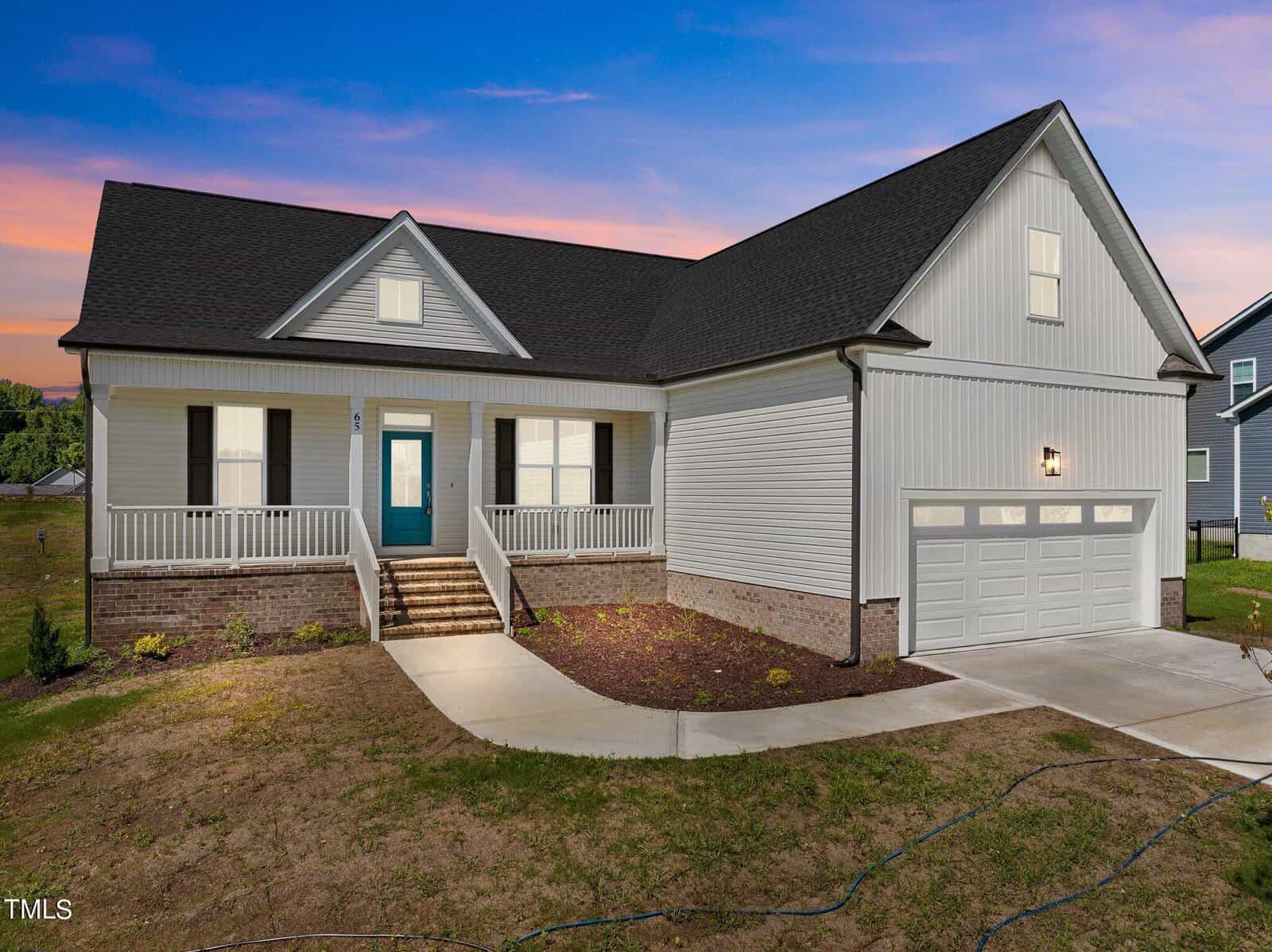A modern single-story house with white siding, dark roof, a teal front door, front porch, double garage, and outdoor lights, shown at dusk with a colorful sky in the background.