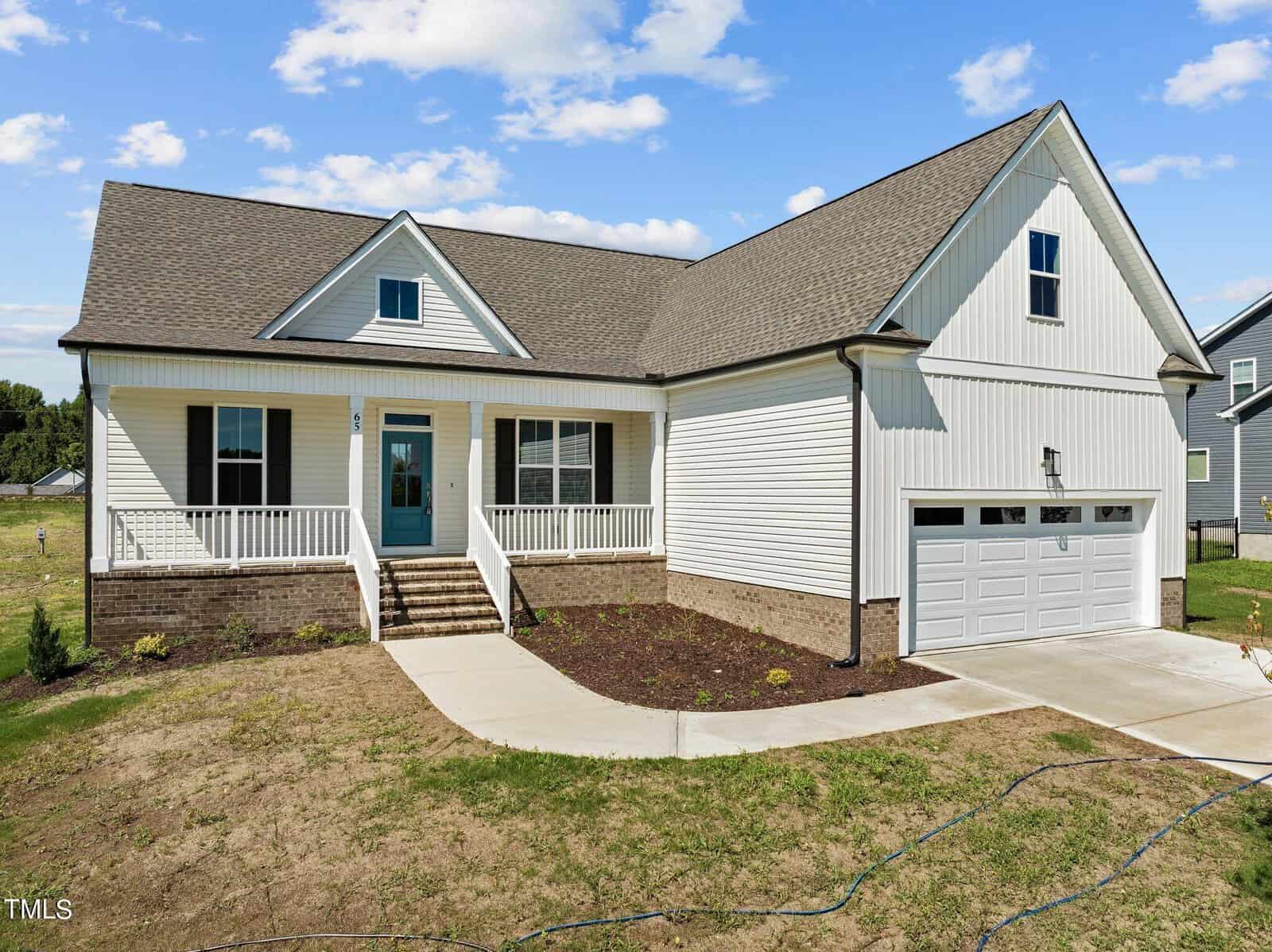 A modern, single-story house with white siding, a covered front porch, two-car garage, and a green lawn under a blue sky with scattered clouds. Steps lead up to a teal front door.