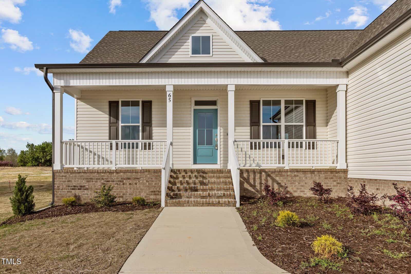 A modern house with beige siding, a blue front door, white trim, a brick foundation, and a covered front porch with white railings. Steps and a walkway lead to the entrance, with sparse landscaping in the front yard.