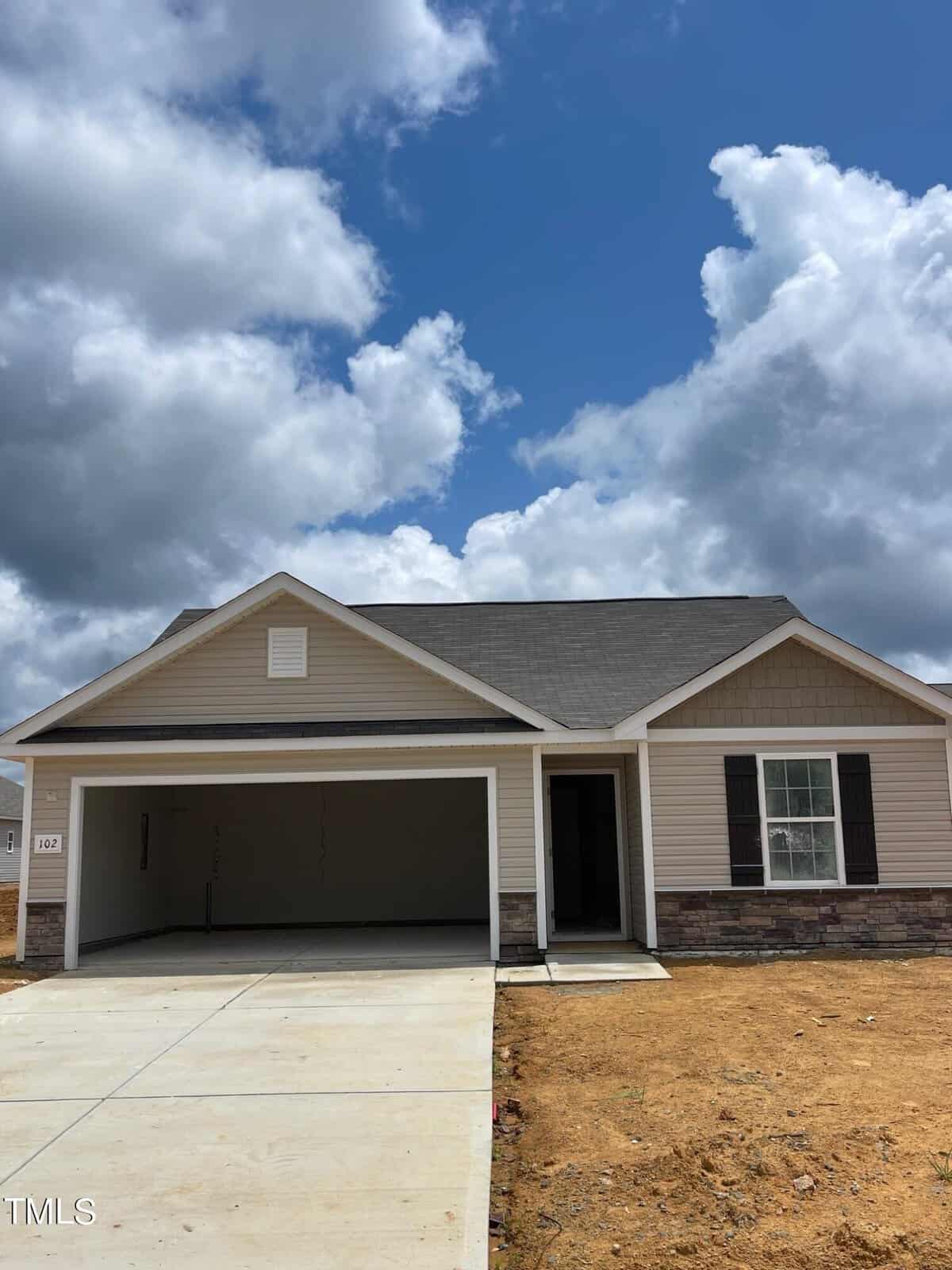 Located at 102 Scoville Street in Oxford, this single-story house boasts a sloped roof and a two-car garage under a partly cloudy sky. With beige siding and stone accents, the new construction features a concrete driveway leading to the garage, surrounded by bare ground.