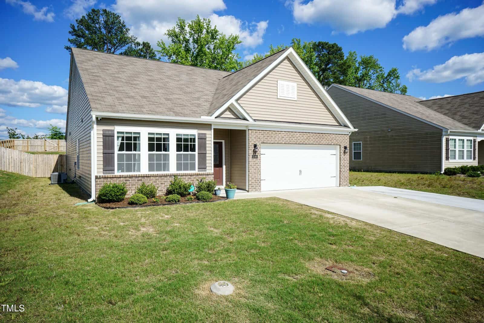Located at 2746 Spring Valley Drive in Creedmoor, this single-story house boasts beige siding and brick accents. It features a two-car garage and a small front yard adorned with a few shrubs. The sloped roof complements the partly cloudy sky above.