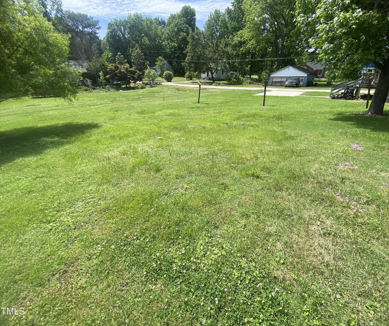 A lush, green grassy lawn under a clear sky with trees and a few houses in the background.