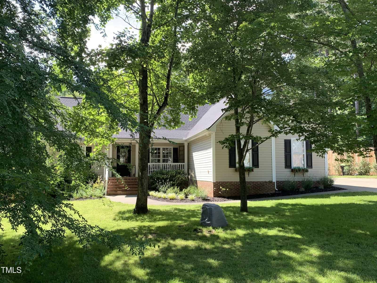 A charming house on 2027 Lonesome Dove Drive features white siding and a brick foundation, surrounded by lush green trees and a well-maintained lawn. Nestled in Franklinton, the serene setting includes a small front porch with steps leading to the welcoming entrance.