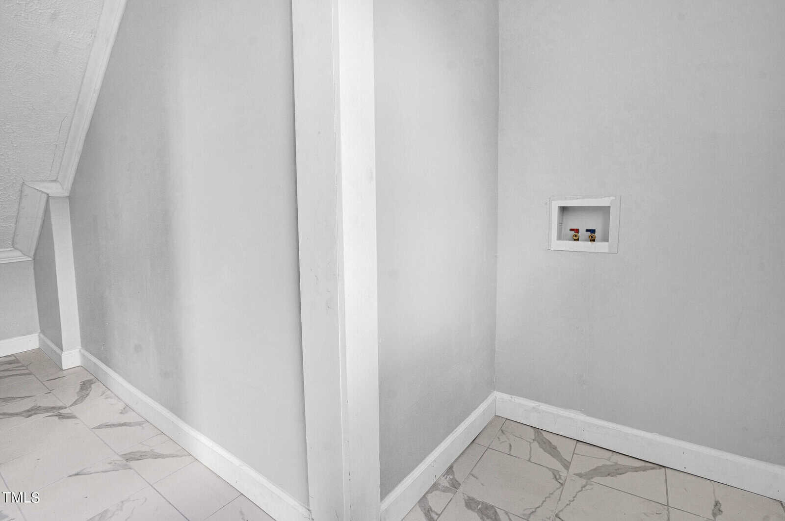 A small nook with a white shelf inset into a gray wall. The floor is tiled with white marbled tiles. The space is bright and minimalist with clean lines and a slight shadow on one side of the wall.