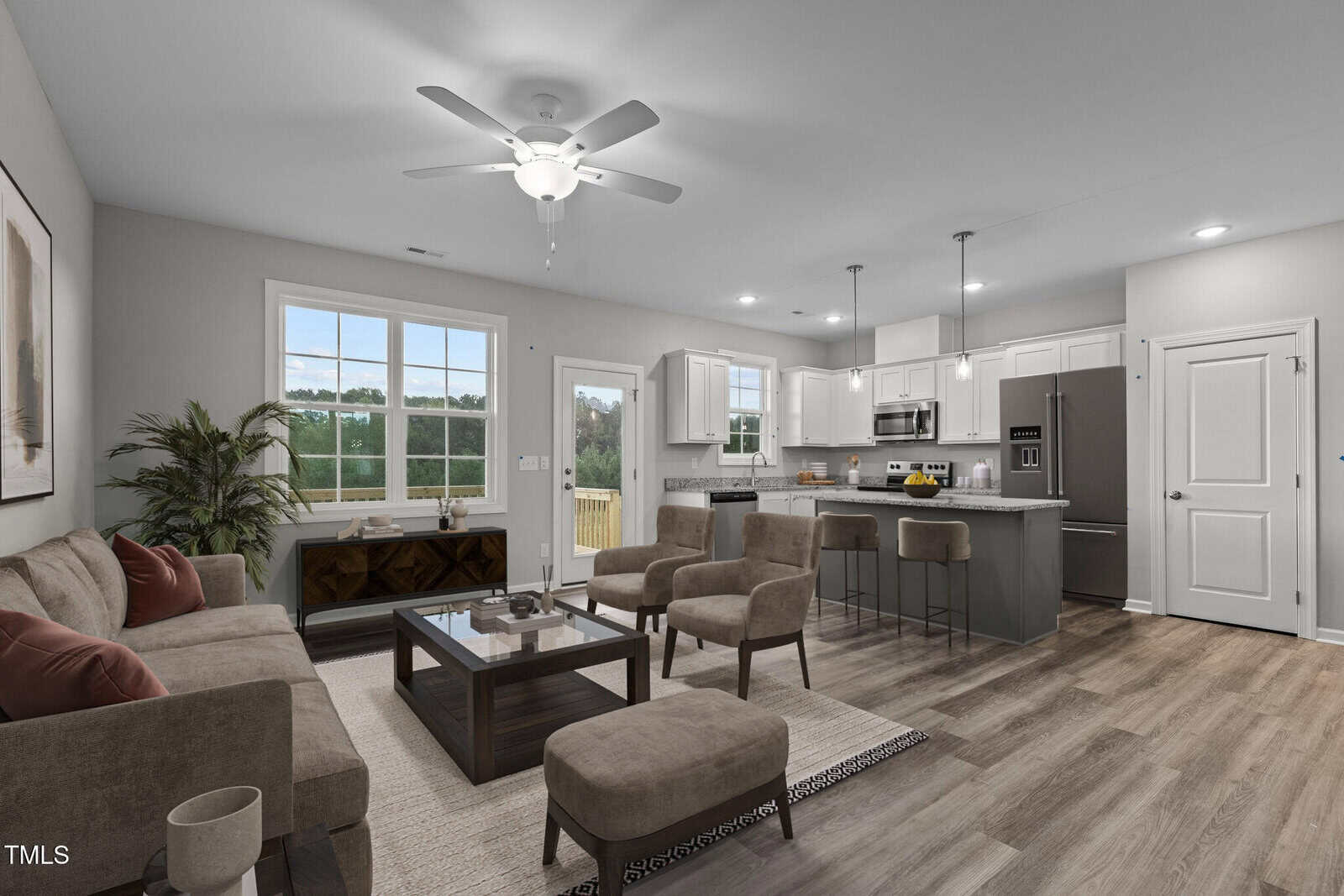 A modern open-concept living room and kitchen with neutral decor, gray cabinets, stainless steel appliances, a large window, a glass door to a deck, a sofa, two chairs, and a dining island with stools.
