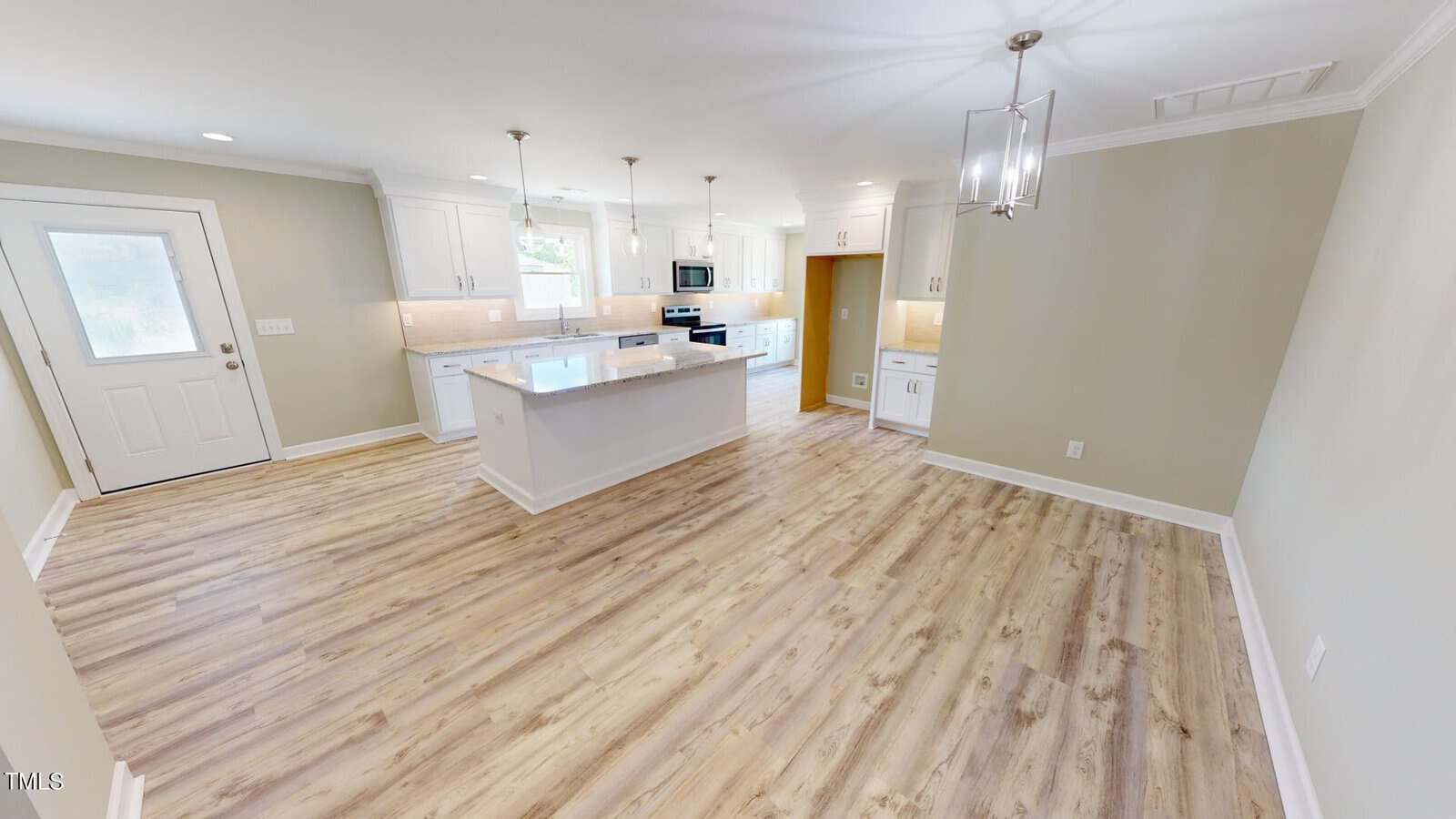 Bright, modern kitchen and dining area with light wood floors, white cabinets, an island, stainless steel appliances, pendant lighting, and neutral-colored walls. A door and multiple windows let in natural light.