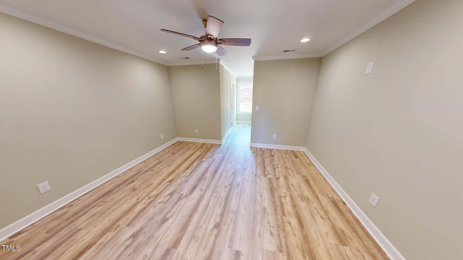 Spacious empty room with light-colored walls, wood-style flooring, a ceiling fan with lights, recessed ceiling lights, and a doorway leading to another area with natural light.