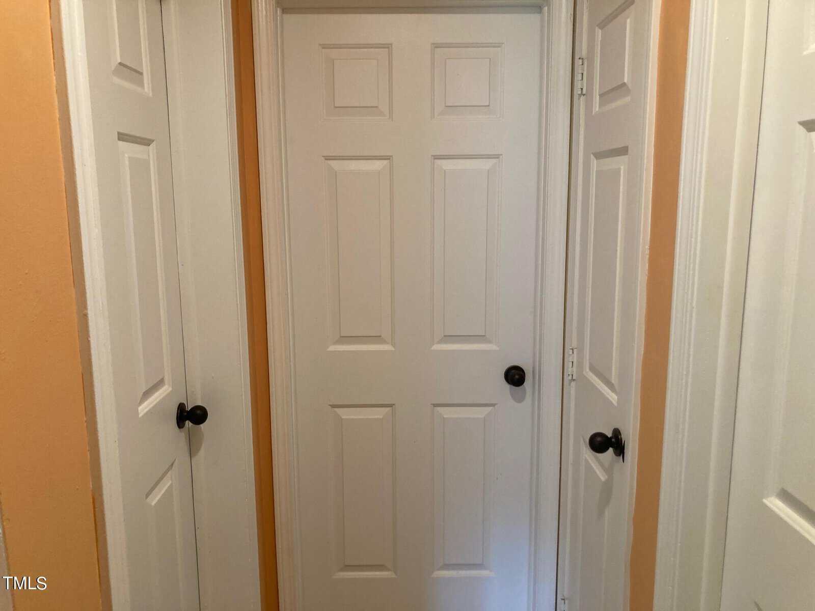 A small hallway with three white doors, each featuring a black doorknob. The walls and trim are painted in a peach color, creating a cozy atmosphere.