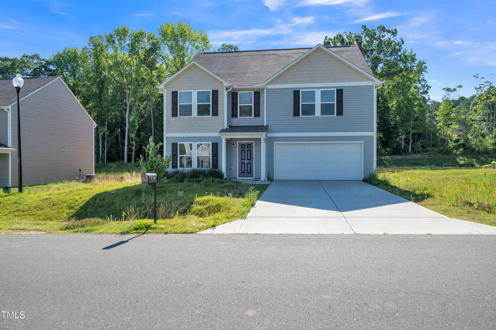 A two-story, gray house with black shutters and a double garage at 350 E Waycliff Road in Henderson, NC. It boasts a neatly maintained front lawn and a wide driveway leading to the garage. The house is situated on a clear, sunny day with a backdrop of trees and greenery.