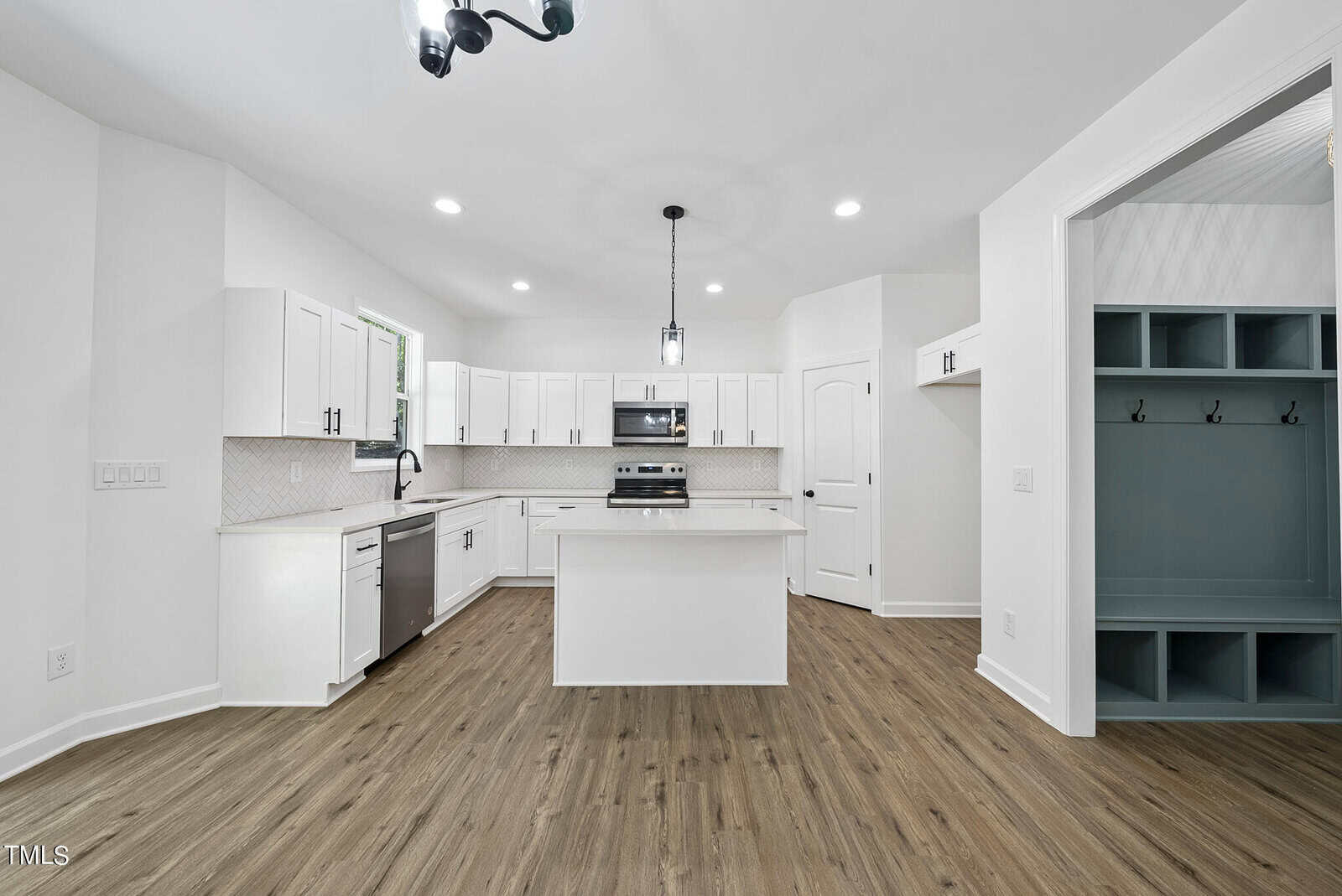 Modern kitchen with white cabinets, stainless steel appliances, central island, tile backsplash, wood-look flooring, and a built-in teal mudroom area with hooks and cubbies on the right.