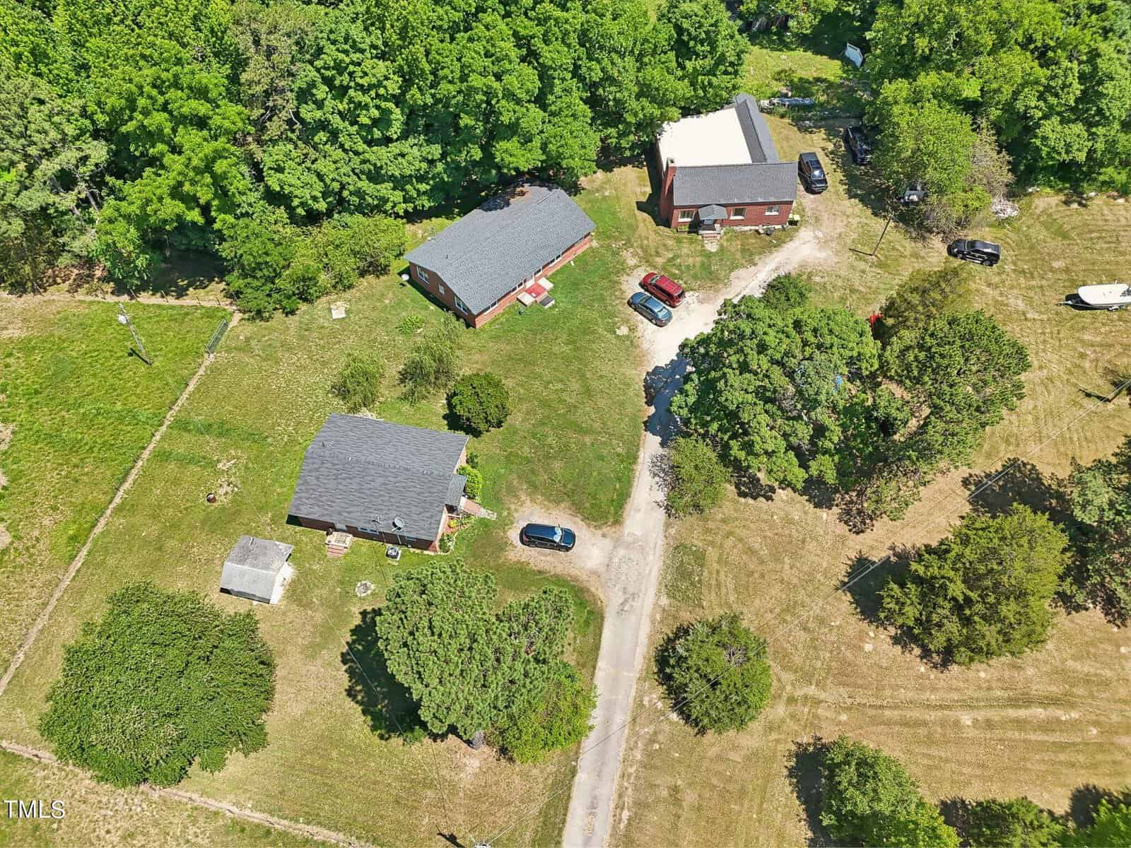 Aerial view of a rural property at 425 Kittrell Road in Kittrell, featuring three buildings surrounded by greenery and trees. The buildings appear to be houses or storage units, with several vehicles parked on a dirt driveway. The area is partially fenced, with grassy fields and scattered shrubs.