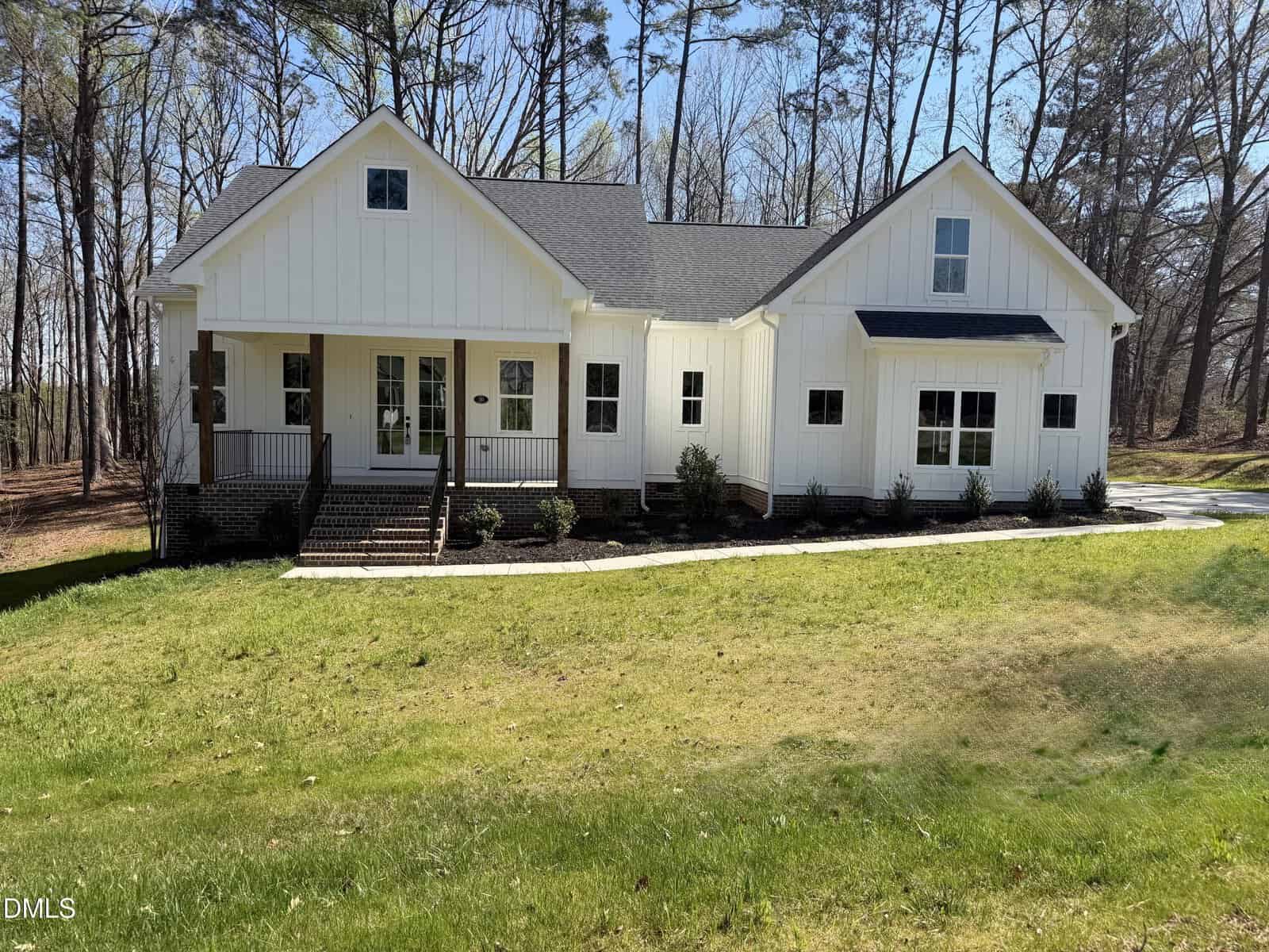 A modern white farmhouse with a black roof at 30 Tamaran Court, featuring large front windows, a covered porch, and steps leading up to the entrance, nestled in a grassy yard with trees in peaceful Spring Hope.