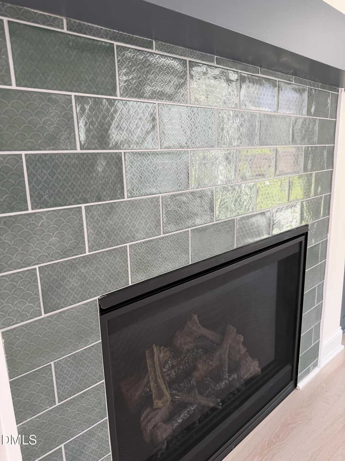 Close-up of a modern fireplace with green rectangular tiles in a staggered pattern, featuring both textured and smooth finishes, and white grout outlining each tile.