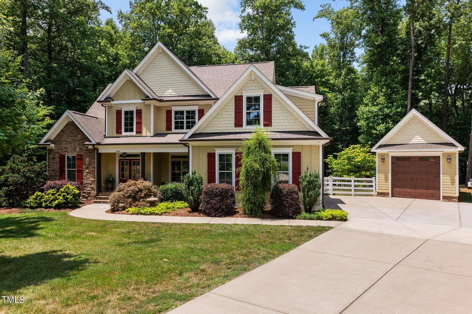 Nestled in Franklinton, this suburban two-story house at 3654 Coughlin Court boasts a beige exterior with red shutters and gabled roofs. To the right, a garage complements the curved driveway, while lush greenery and trees embrace the property under the sunny sky.