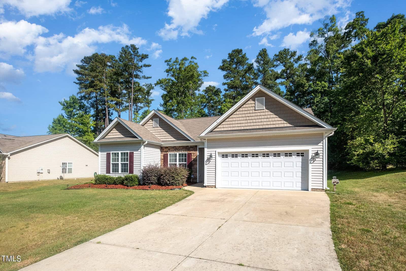 Located at 205 Griffis Drive, this suburban, single-story house boasts a gray roof and beige siding. It features a double garage and a well-kept lawn adorned with shrubs. Tall trees stem from the backdrop under a blue, cloudy sky.