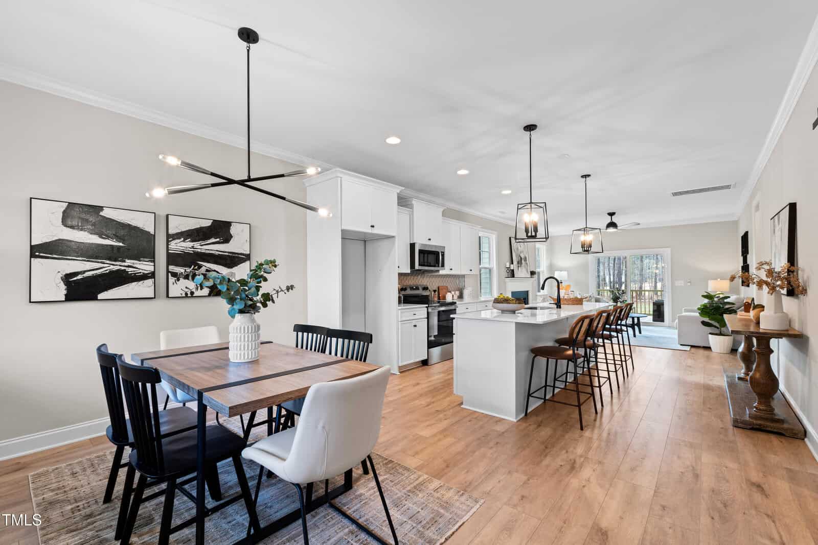 Modern open-concept kitchen and dining area with wood floors, a rectangular dining table with black and white chairs, white cabinetry, a kitchen island with bar stools, and abstract art on the walls.