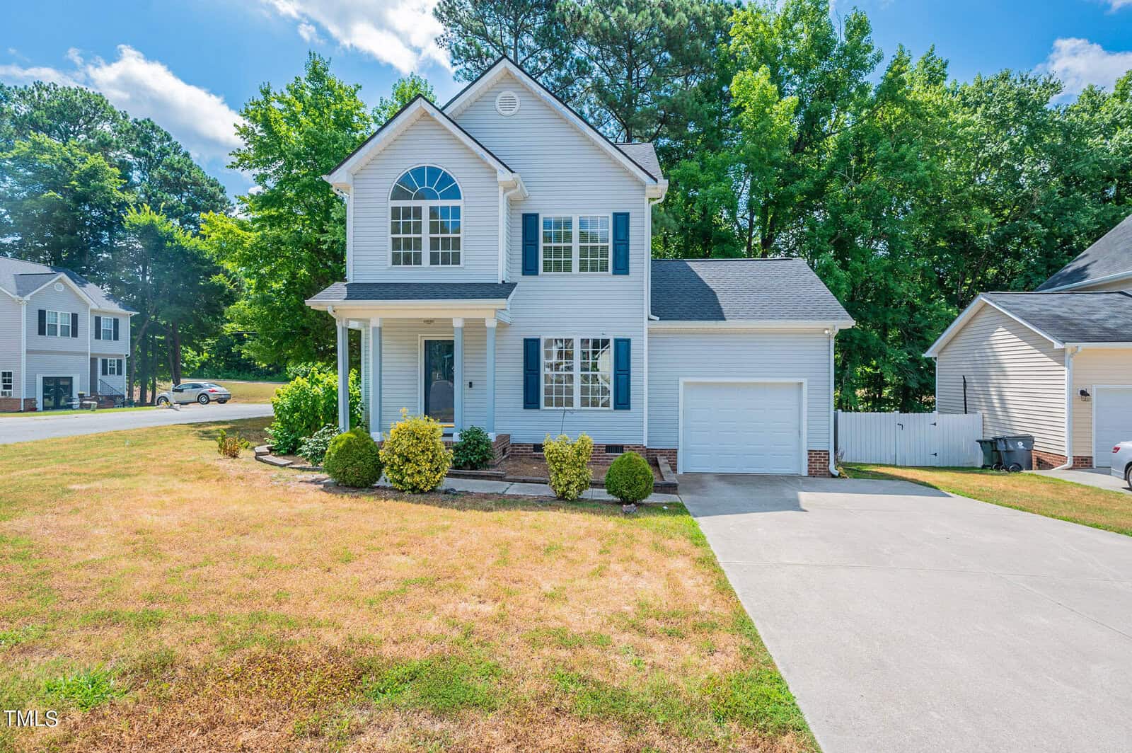 Located at 201 Korbin Court in Creedmoor, this charming two-story house boasts light blue siding, a gabled roof, and a single-car garage. The inviting front porch overlooks a manicured lawn with shrubs, set in a picturesque suburban neighborhood beneath a clear blue sky.