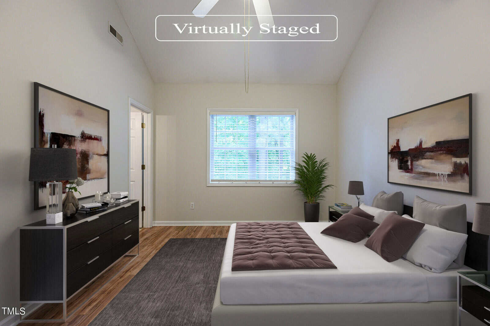 Virtually staged bedroom with a neatly made bed, two abstract paintings on the walls, a dark dresser, and a window with blinds letting in natural light. A ceiling fan hangs above, and a potted plant sits in the corner.