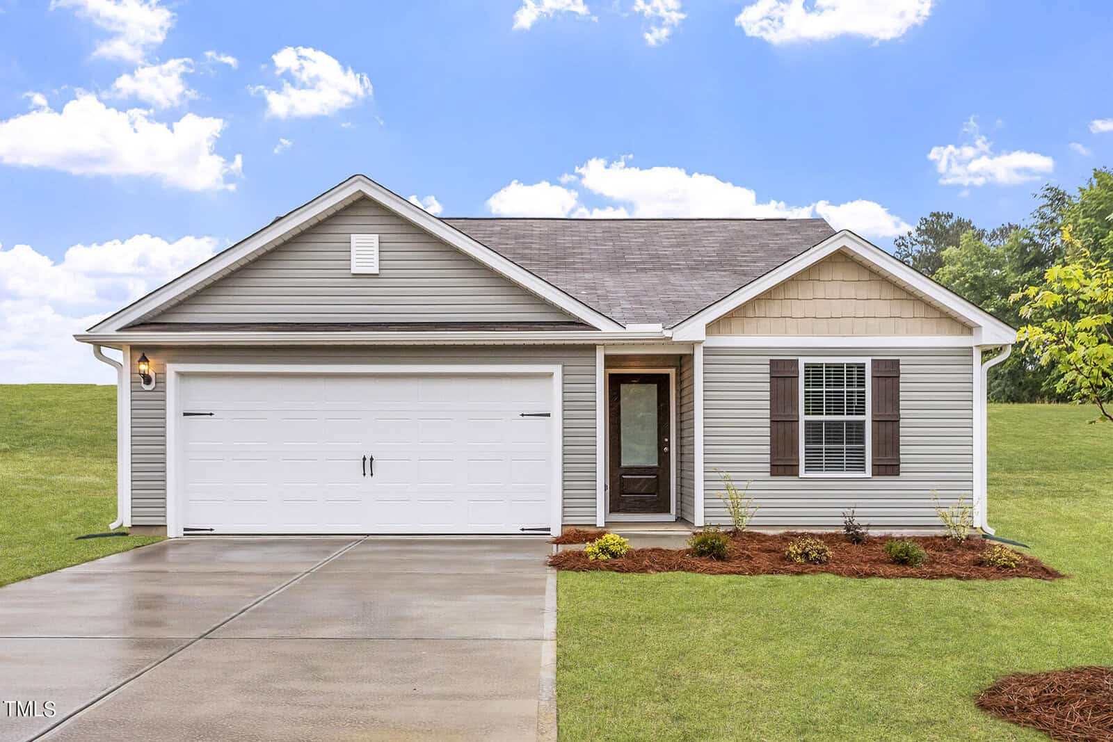 A single-story house on 100 Anaheim Street with gray siding and a shingle roof, featuring a white garage door and a dark front door with a window. The Oxford-style home has minimal landscaping, small shrubs, and a neat lawn against green trees and blue sky.